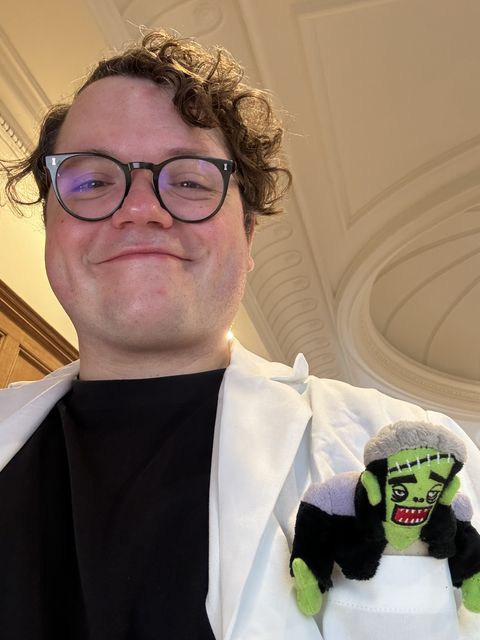 Picture of me in a white lab coat with a Frankenstein plushie in my top left pocket
