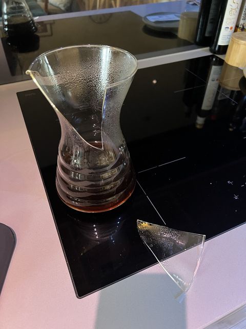 Photograph of a v60 carafe coffee make half full of coffee with a giant crack and a broken off piece of glass next to it.